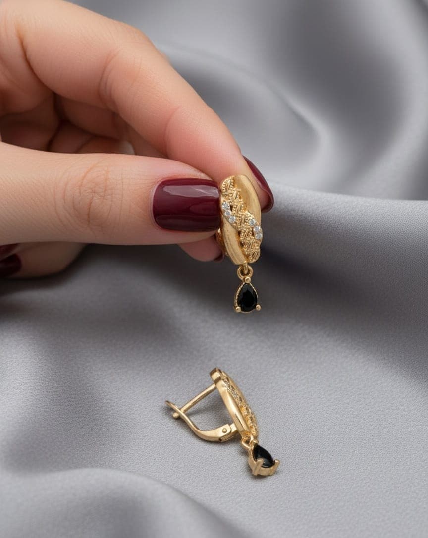 A delicate gold-plated earring featuring a distinctive feather design and sparkling zircon stones, with an elegant black zircon piece hanging from it. Clip-Ons (5)