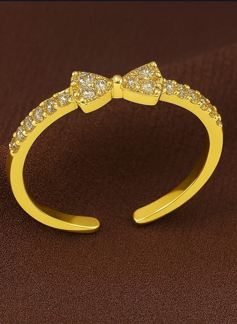"Elegance exudes delicacy - An open design ending with an elegant knot, combining fluidity with a sophisticated artistic touch. Delicate details add a dimension of distinction, while the pavé setting on the half ring lends a soft, eye-catching radiance. Ideal for everyday looks or special occasions, it reflects a refined feminine taste." Women's Rings (٥)
