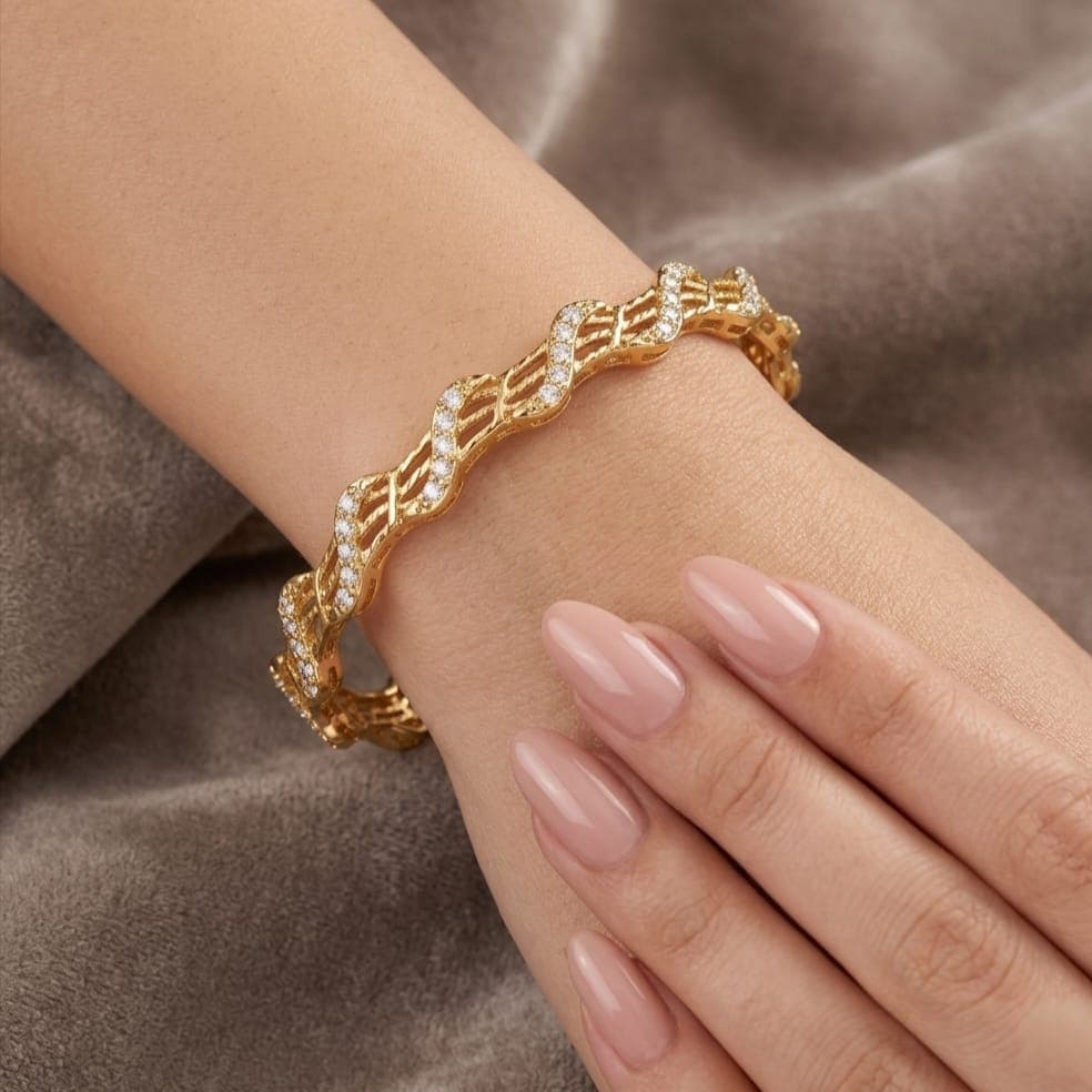 An elegant gold-tone bracelet with a flowing, wavy design that blends luxury and simplicity. Adorned with sparkling zircon stones and delicate engravings, it adds a touch of beauty to your look. Women's Bangles